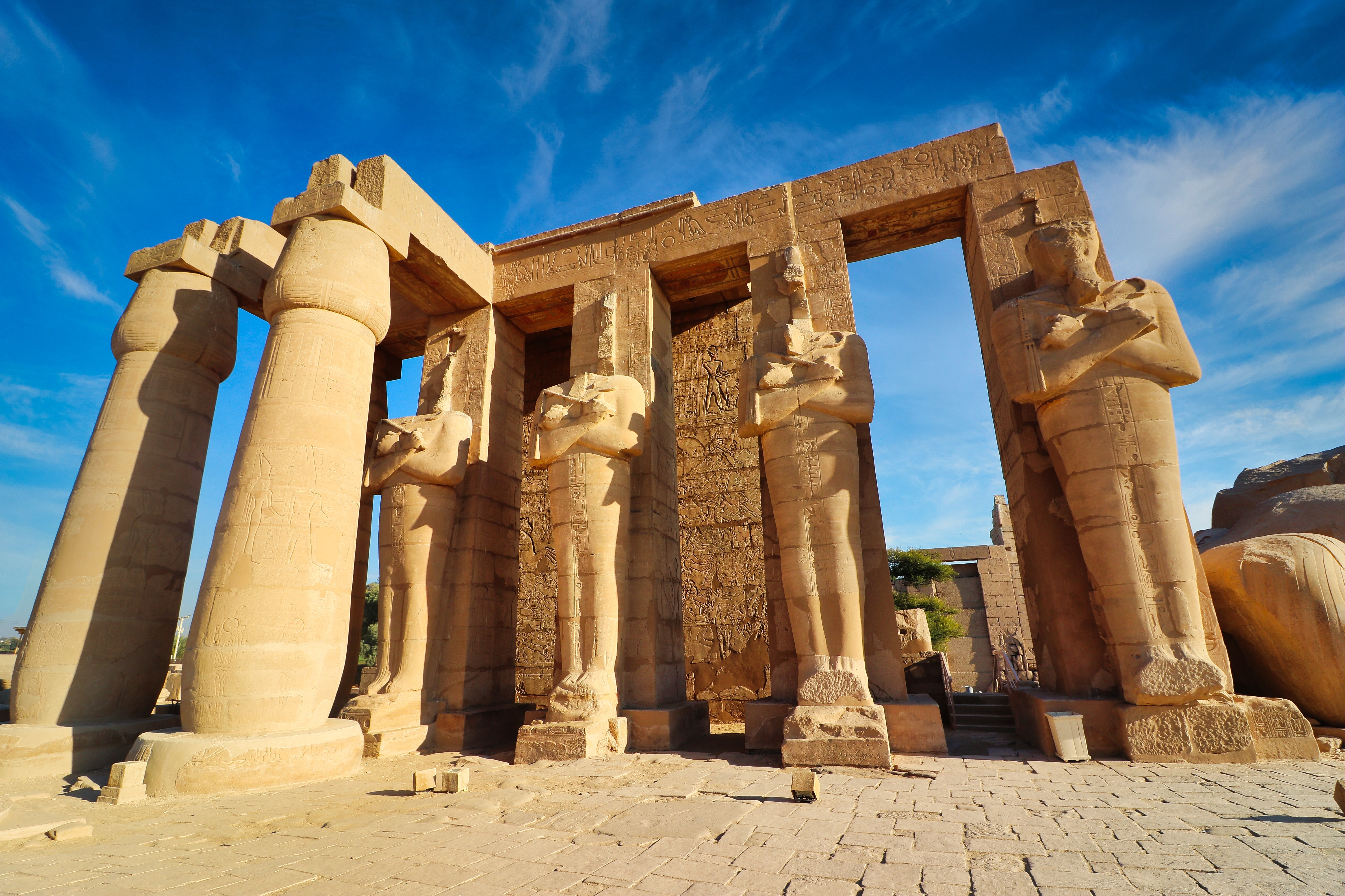 View of the Ramesses statues at the entrance to the Ramesseum, the Mortuary Temple of Pharoah Ramesses II the Great on a bright afternoon with blue skies at Luxor, Egypt